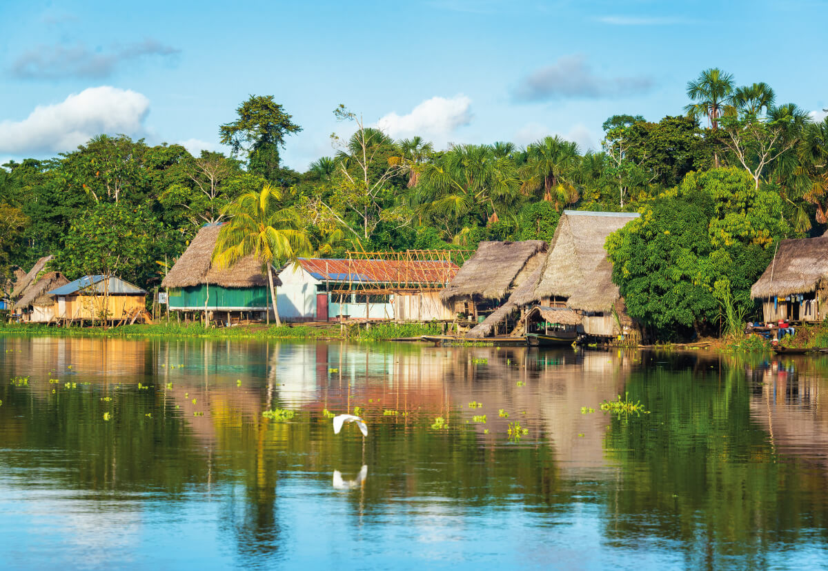 Casas junto a un río amazónico, con palmas y reflejo en el agua